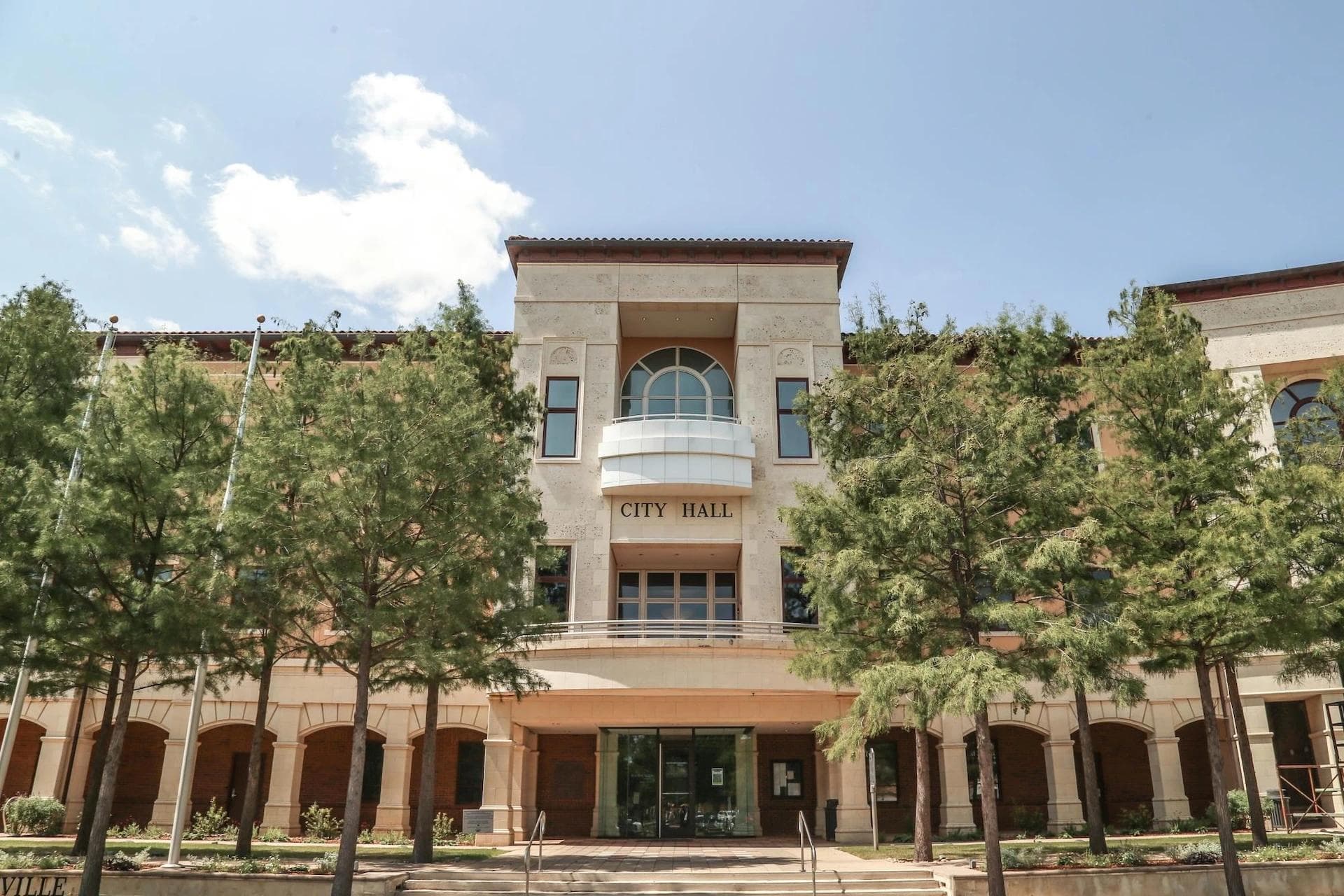 Front view of Colleyville City Hall surrounded by trees under a bright sky.